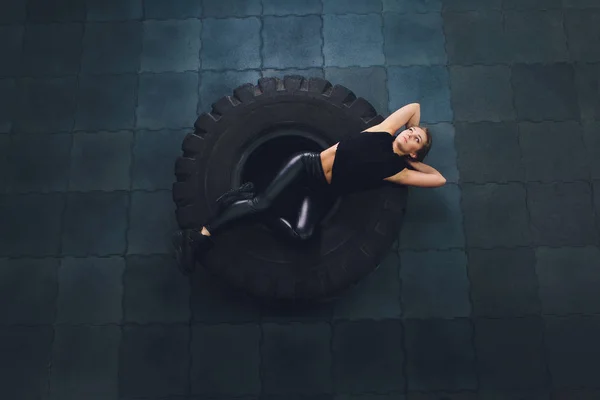Potente, attraente ragazza muscolosa impegnata in palestra, allenamento con pneumatici giganti in palestra. Atleta a riposo dopo un duro allenamento. Esercizio con pesi elevati in palestra . — Foto Stock