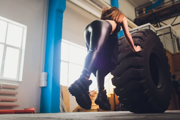 Ženský atlet, pracující s obrovskou pneumatkou, se otáčí a nosí v tělocvičně. žena cvičujících s velkým pneumatika. — Stock fotografie