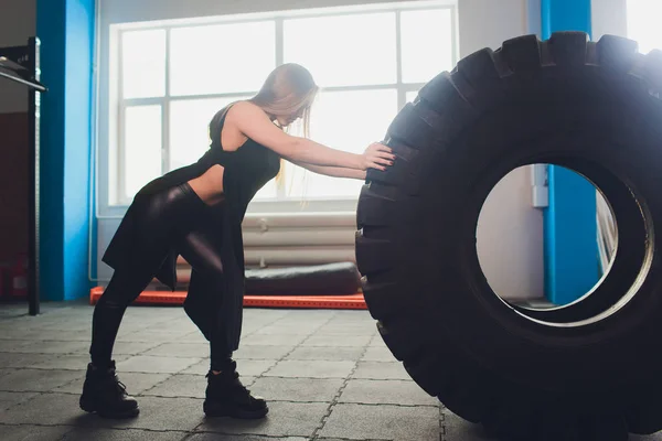 Fit női sportoló dolgozott ki egy hatalmas gumiabroncs, esztergálás és folytatni az edzőteremben. nő gyakorló nagy gumiabroncs. — Stock Fotó