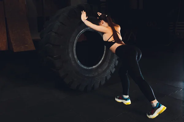 Mulher fitness lançando pneu de roda no ginásio. Apto atleta feminino trabalhando com um pneu enorme. Vista traseira. Desportista fazendo um treinamento de exercícios de força . — Fotografia de Stock