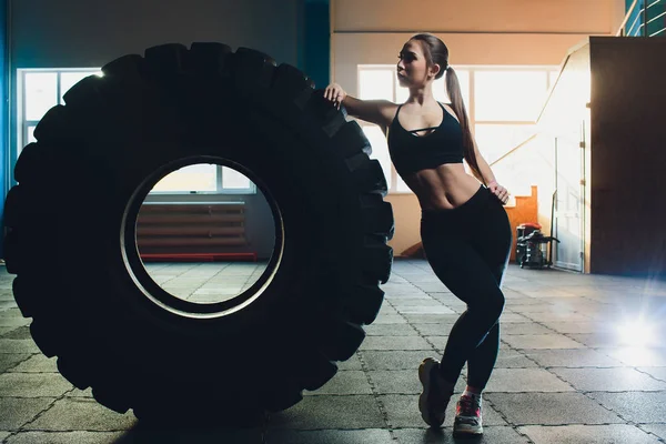 Mulher fitness lançando pneu de roda no ginásio. Apto atleta feminino trabalhando com um pneu enorme. Vista traseira. Desportista fazendo um treinamento de exercícios de força . — Fotografia de Stock