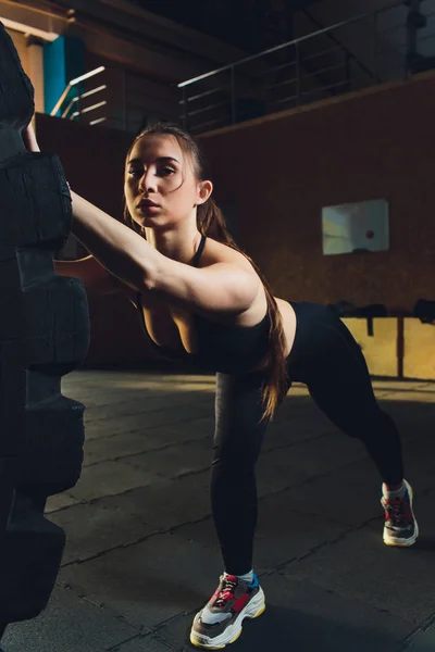 Fitness dziewczyny rzut koła opony w siłowni. Dopasowanie lekkoatletka wypracowania z ogromne opony. Widok z tyłu. Sportsmenka siłowego Ćwiczenia szkoleniowe. — Zdjęcie stockowe