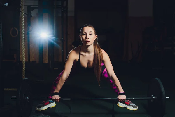 Een mooie sport meisje traint een biceps met een staaf in haar handen in de sportschool. — Stockfoto