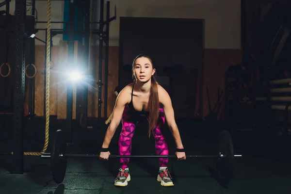 Een mooie sport meisje traint een biceps met een staaf in haar handen in de sportschool. — Stockfoto