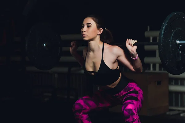 Una hermosa chica deportiva entrena un bíceps con una varilla en las manos en el gimnasio . — Foto de Stock