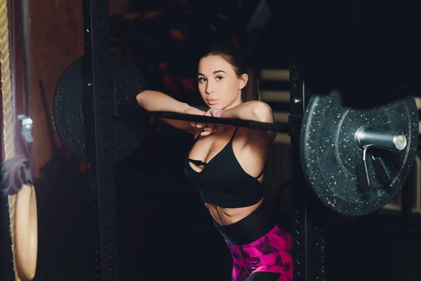 Seorang gadis olahraga yang cantik melatih bisep dengan tongkat di tangannya di gym . — Stok Foto