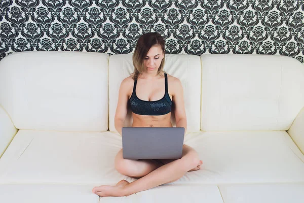 Rahat kanepe, ev iç otururken dizüstü bilgisayar kullanan genç kadın.