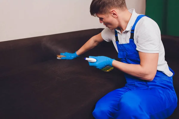 Περικομμένη εικόνα. Η ιδέα του καθαρισμού. Αρσενικό χέρι σε μπλε προστατευτικά γάντια καθαρισμό καναπέ καναπές στο δωμάτιο. — Φωτογραφία Αρχείου