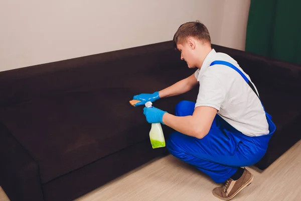 Обрезанное изображение. Концепция очистки. Мужская рука в синих защитных перчатках чистит диван в комнате . — стоковое фото