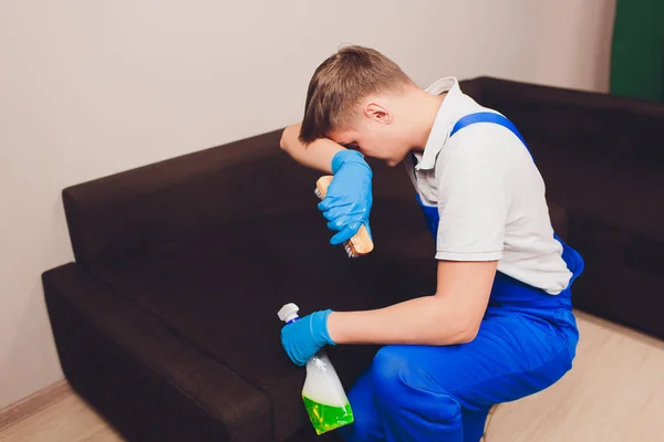 Ένας κουρασμένος νεαρός που κάθεται στον καναπέ στο σαλόνι. απορροφητήρας, Καναπές, χημεία, Πλύσιμο, καθάρισμα. Γάντια προστασίας από μπλε — Φωτογραφία Αρχείου