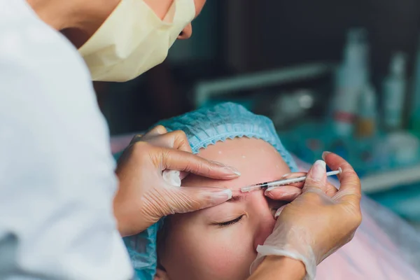 Лікар дає ін'єкції для ліфтингу обличчя жінці середнього віку в лобі між бровами, щоб видалити експресійні зморшки в клінічній хірургічній кімнаті фону O.R. — стокове фото