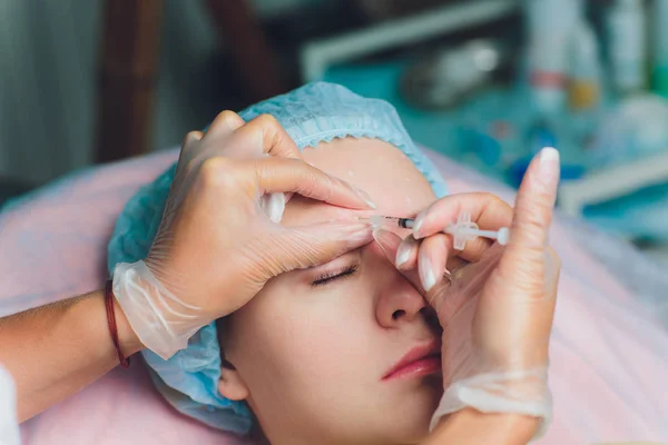 Doctor giving face lifting injection on mid age woman in the forehead between eyebrows to remove expression wrinkles in a clinic surgery room O.R background Beautify filler for face anti aging concept