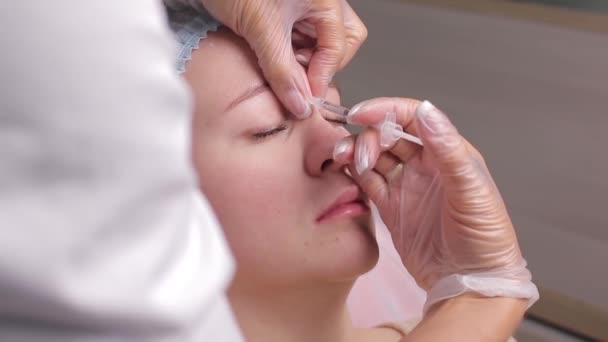 Médico que da inyección de lifting facial en mujer de mediana edad en la frente entre las cejas para eliminar las arrugas de expresión en una sala de cirugía clínica. — Vídeos de Stock