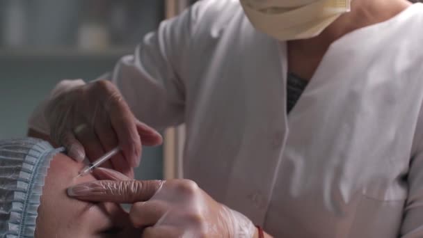 Médico dando cara levantando injeção na mulher de meia idade na testa entre as sobrancelhas para remover rugas de expressão em uma clínica sala de cirurgia fundo O.R embelezar enchimento para rosto conceito anti envelhecimento — Vídeo de Stock