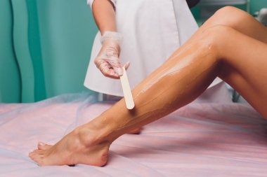 Şevval Özçelik Güzellik epilasyon için hazırlanıyor ve balmumu sopayla krema güzel kadın ayak üzerinde uygulama. Güzellik Salonu.