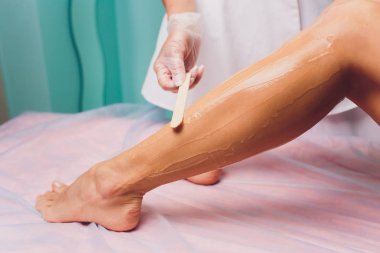 Şevval Özçelik Güzellik epilasyon için hazırlanıyor ve balmumu sopayla krema güzel kadın ayak üzerinde uygulama. Güzellik Salonu.