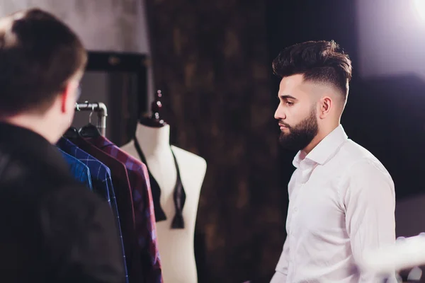 Mężczyzna klienta w centrum handlowym próbuje ubrania biznesowe, asystent sklepu pomagając klientowi. — Zdjęcie stockowe