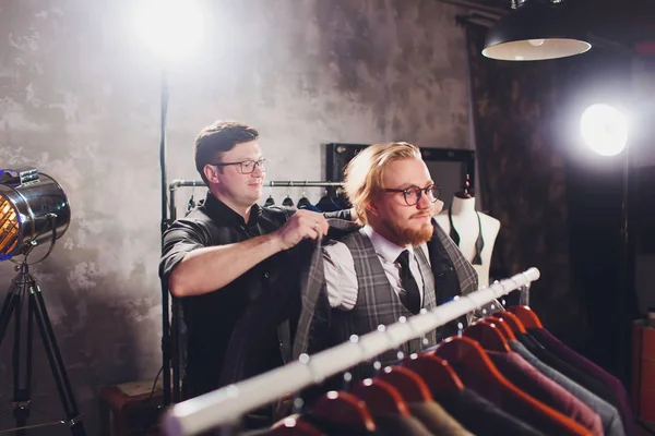 Αρσενικό πελάτης στο εμπορικό κέντρο προσπαθεί επαγγελματικά ρούχα, βοηθός καταστήματος βοηθώντας τον πελάτη. — Φωτογραφία Αρχείου