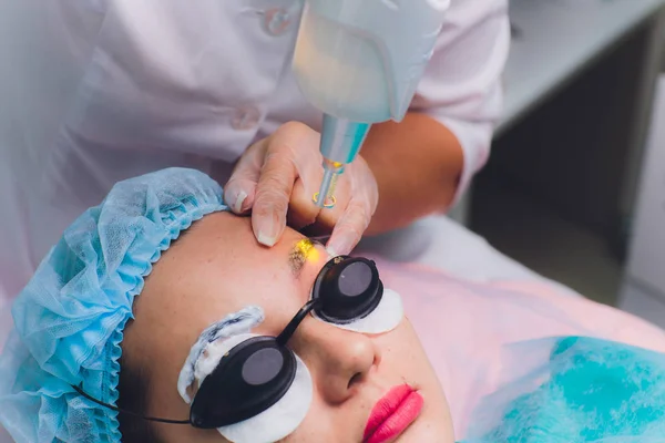 Лазерное удаление перманентного макияжа на лице. Крупный план молодая женщина получает исправление татуировки на брови процедуры. Коррекция естественных недостатков на лице . — стоковое фото