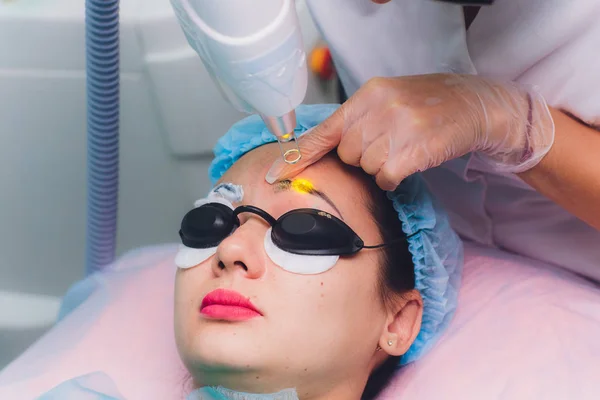 Лазерное удаление перманентного макияжа на лице. Крупный план молодая женщина получает исправление татуировки на брови процедуры. Коррекция естественных недостатков на лице . — стоковое фото