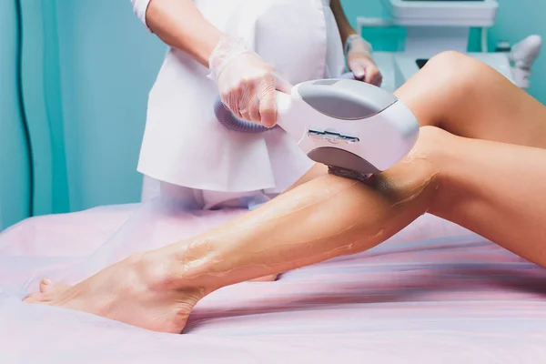 Kosmetyczka usuwa włosy na pięknych kobiecych nogach za pomocą lasera. depilacja nóg, zabieg laserowy w klinice. — Zdjęcie stockowe