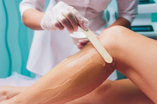 Kosmetyczka jest przygotowanie do depilacji i stosowania kremu z drążka wosku na piękne kobiece nogi. Salon piękności. — Zdjęcie stockowe
