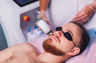Young Man Receiving Laser Hair Removal Treatment At Beauty Center. clipart