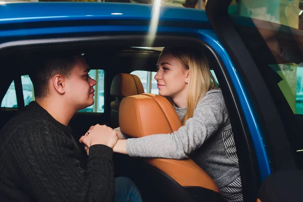 Tomando su decisión. Hermosa pareja amorosa sentada en un coche nuevo juntos en el concesionario hombre guapo y su novia amorosa elegir un coche juntos vehículo de consumismo . —  Fotos de Stock