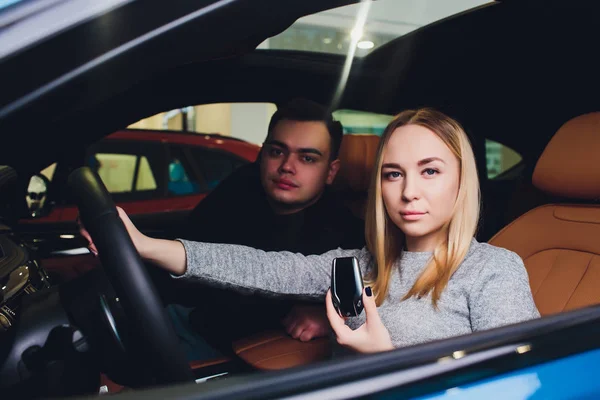 Tomando a decisão deles. Belo casal amoroso sentado em um carro novo juntos na concessionária homem bonito e sua namorada amorosa escolher um carro juntos veículo consumismo . — Fotografia de Stock