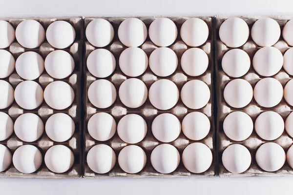 Ovos brancos de uma galinha em embalagem inofensiva, de papelão em um fundo branco. — Fotografia de Stock