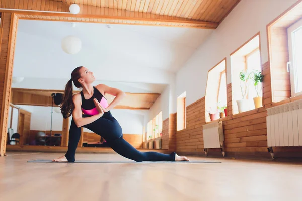 Joven mujer yogui atractiva practicando yoga, de pie en el ejercicio Parsvrtta Parsvakonasana, pose de ángulo lateral giratorio, haciendo ejercicio, usando ropa deportiva, estilo urbano fresco . — Foto de Stock