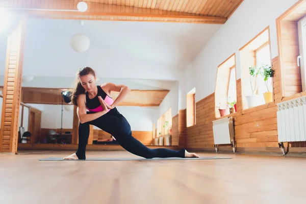 Joven mujer yogui atractiva practicando yoga, de pie en el ejercicio Parsvrtta Parsvakonasana, pose de ángulo lateral giratorio, haciendo ejercicio, usando ropa deportiva, estilo urbano fresco . — Foto de Stock