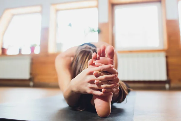 Joven mujer atractiva deportista practicando yoga, haciendo ejercicio Giratorio de la cabeza a la rodilla hacia adelante, pose de Parivrtta Janu Sirsasana, haciendo ejercicio, usando ropa deportiva, pantalones negros, primer plano interior, estudio de yoga . — Foto de Stock