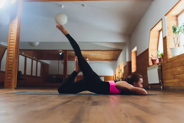 Giovane donna sportiva che pratica yoga, facendo esercizio di calci a doppia gamba, posa Salabhasana, esercizio, indossare abbigliamento sportivo, pantaloni grigi e top, close up indoor, studio di yoga . — Foto Stock