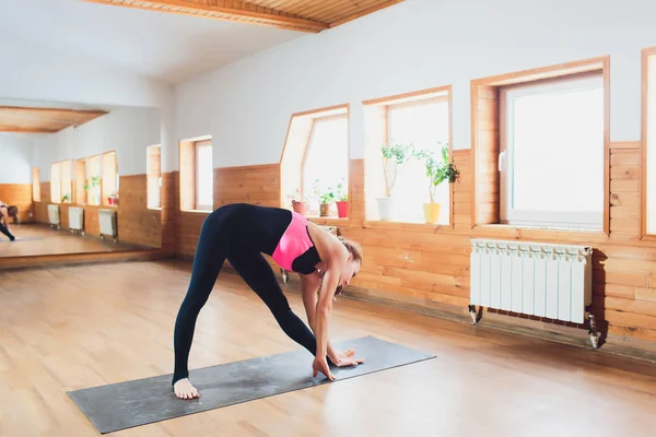 Junge attraktive Frau praktiziert Yoga, steht in drehbarem Dreieck, parivrrta trikonasana Pose, trainiert in Sportbekleidung, drinnen in voller Länge, isoliert vor Studiohintergrund. Stockbild