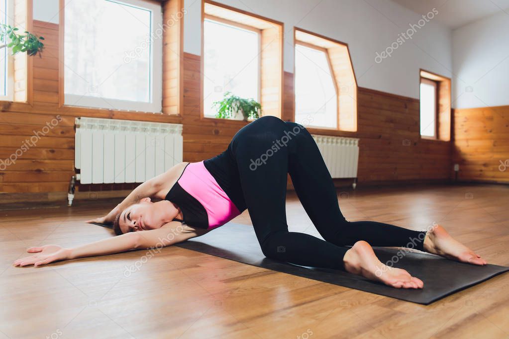 Young attractive woman practicing yoga, doing asana paired with Cow Pose on the inhale, Cat exercise, Marjaryasana pose, working out, wearing sportswear, grey pants, top, indoor full length, studio.