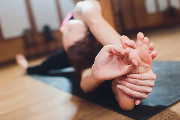 Primer plano de una chica haciendo una asana inclinándose hacia adelante con las manos hacia sus piernas. Sentado en el suelo sobre una esterilla de yoga rosa. Agarra los pies. Puntos Marma . — Foto de Stock