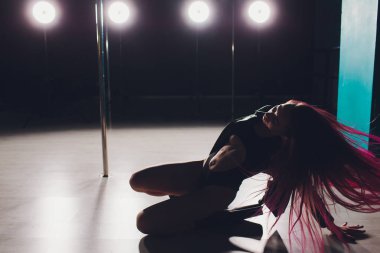 Kırmızı saçlı kutup dans kız egzersizleri ve siyah arka plan üzerinde duman pilon üzerinde pozlar.