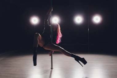 Kırmızı saçlı kutup dans kız egzersizleri ve siyah arka plan üzerinde duman pilon üzerinde pozlar.