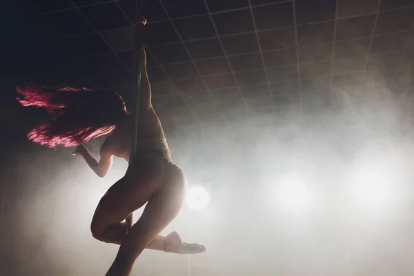 Rojo de pelo pole dance chica ejercicios y poses en el pilón en el humo en el fondo negro . — Foto de Stock