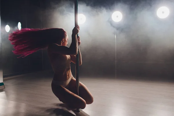 Rosso dai capelli pole dance ragazza esercizi e pose sul pilone nel fumo sullo sfondo nero . — Foto Stock