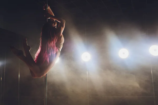 Jeune femme mince pole dance dans l'intérieur sombre avec des lumières et de la fumée . — Photo