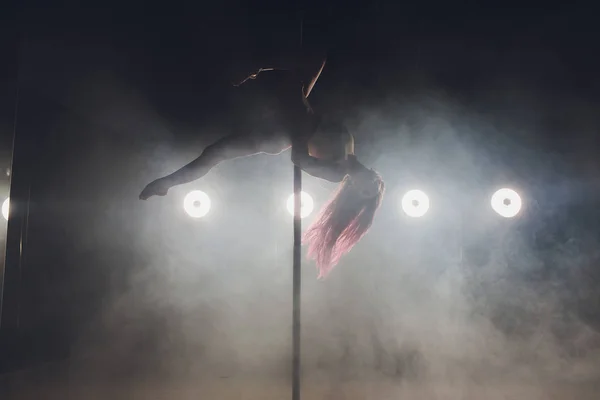 Young slim woman pole dancing in dark interior with lights and smoke. — Stock Photo, Image