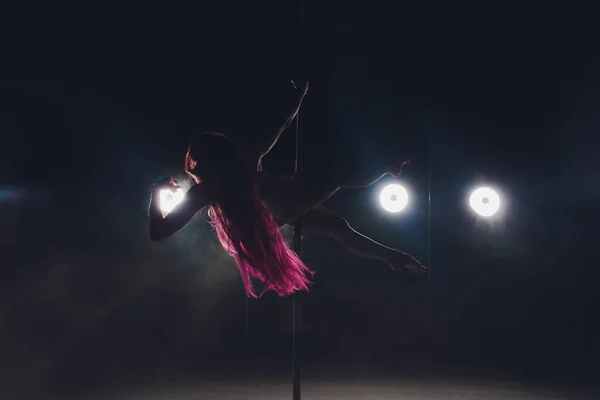Jeune femme mince pole dance dans l'intérieur sombre avec des lumières et de la fumée . — Photo