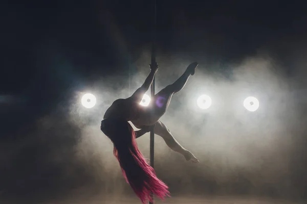 Νεαρή λεπτή γυναίκα πόλο χορεύει σε σκοτεινό εσωτερικό με φώτα και καπνό. — Φωτογραφία Αρχείου