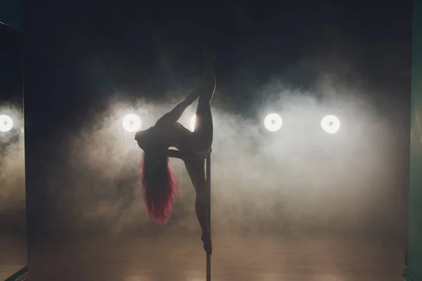 Молода струнка жінка полюс танцює в темному інтер'єрі з вогнями і димом . — стокове фото