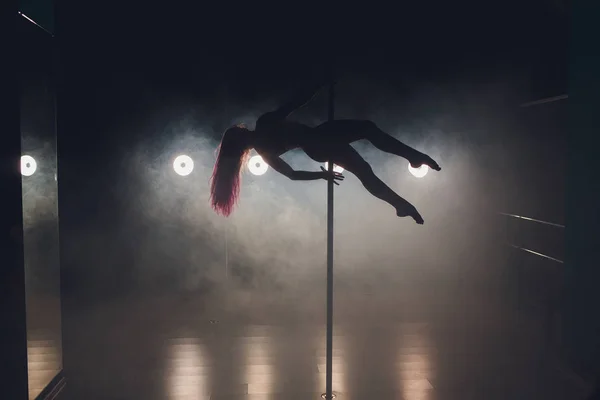 Jeune femme mince pole dance dans l'intérieur sombre avec des lumières et de la fumée . — Photo