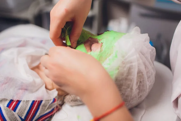 Cosmetólogo con la ayuda de un cepillo de maquillaje especial hace una máscara de spa terapéutica de algas verdes contra el envejecimiento de una mujer joven . — Foto de Stock