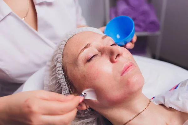 Schöne junge Frau mit einer kosmetischen Gesichtsmaske im Spa-Salon. Mädchen befindet sich in kosmetischer Behandlung. — Stockfoto