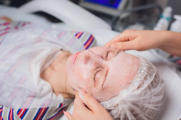 Schöne junge Frau mit einer kosmetischen Gesichtsmaske im Spa-Salon. Mädchen befindet sich in kosmetischer Behandlung. — Stockfoto